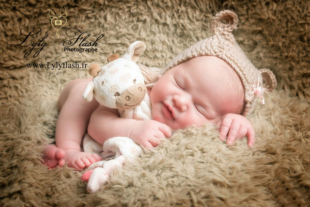 photo d une petite fille à sa séance photo naissance avec son doudou, un bonnet et un joli sourire de bonheur