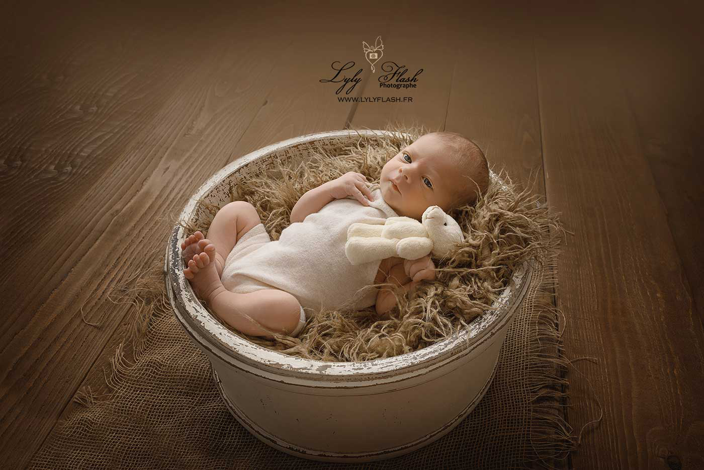 photo de bébé a la naissance dans un beau panier en bois, qui regarde la beauté de la lumière naturelle qui vient réchauffer la scène