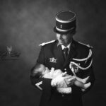 Un papa gendarme tient dans ses bras sa petite fille d'un mois, une magnifique photographie en noir et blanc qui montre toute l'implication de la famille dans le métier de papa si important a notre monde. la Force et la douceur du héro.