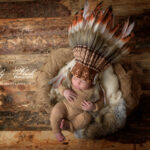 Un magnifique petit bébé indien pose avec des plumes sur la tête, et dans un décor d'indien antique, une photographie pour la naissance de ce bébé réalisée par la photographe Lyly Flash pour cette famille de Hyères