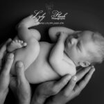 un bébé en position de la grenouille c'est endormi dans les mains de ses parents qui lui créer un berceau d'amour, photographie en noir et blanc