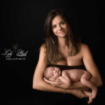 une magnifique jeune maman de Cabasse pose avec son nouveau-né au studio de la photographe Lyly Flash, Elle porte une robe tube noir qui ce fond avec le décor