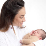 une jeune maman portant un haut blanc sur un fond blanc studio , tient son fils dans ses bras avec un sourire de bonheur. Une photo souvenir magnifique réalisée par la photographe spécialisée dans la photo de naissance près de La Bastide dans le var