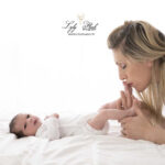 photo de naissance pour une famille de Saint-Martin-de-Pallières. Le bébé est allongé sur le lit et la maman lui embrasse les pieds. Un moment de tendresse capturé par la photographe dans le home studio