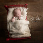 un bébé né a Noël le 24 décembre pose au studio photo dans son petit lit Rouge et tient dans ses mains un petit bonhomme de neige. une photographie pour rappeler sa saison de naissance et mettre en valeur cette date si spéciale. Photographie réalise par la photographe spécialisée du bébé dès la naissance pour un petit prince de Saint-Raphaël