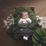 Un bébé nouveau-né en pyjama blanc dort dans un panier en osier sur un fond en bois vintage pour une décoration douce et estivale. photographie réalisée pour une famille de Salon-de-Provence par la photographe Lyly flash