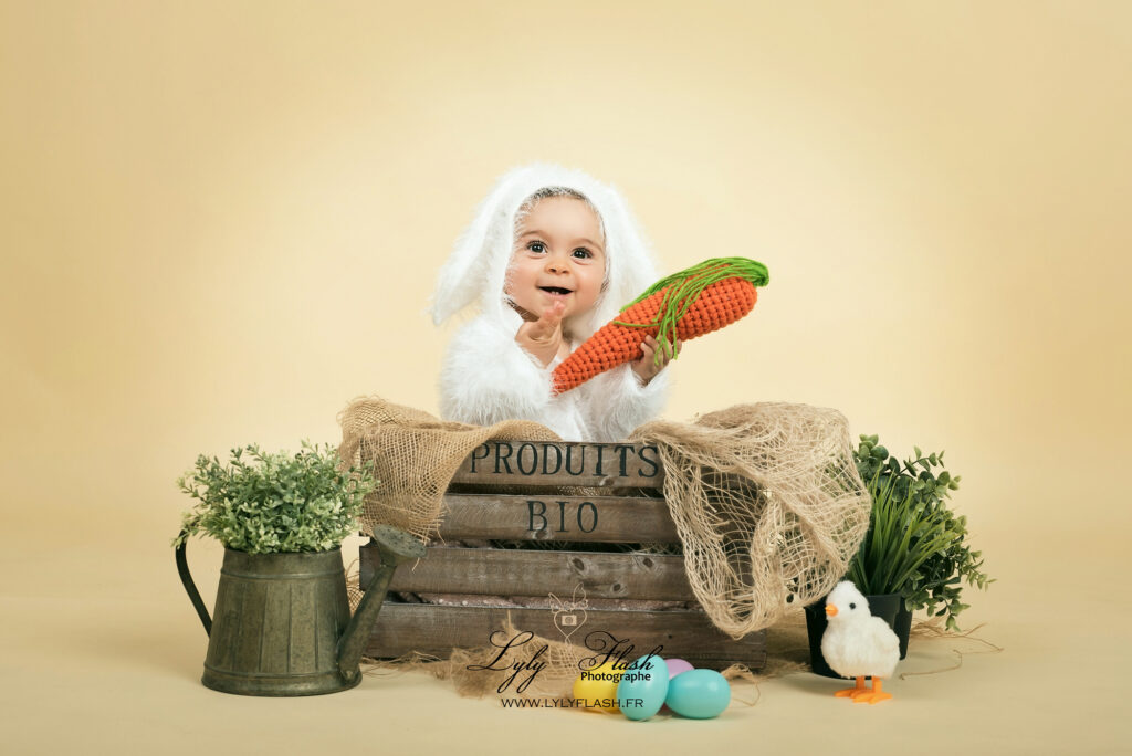 photo portrait d un bébé de 12 mois pour célébrer pâques au studio photo. Il est trop mignon avec sa tenue de petit lapin blanc et son grand sourire qui met en valeur ses deux petits dents de lait