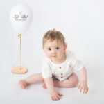 Photo anniversaire un bébé avec une belle tenue blanche et son ballon blanc pose devant la photographe de Brignoles