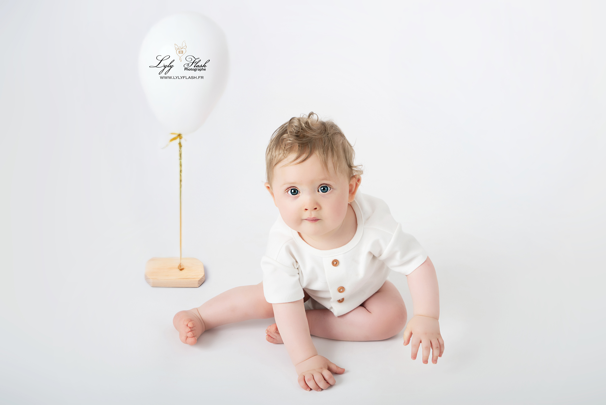 Photo anniversaire un bébé avec une belle tenue blanche et son ballon blanc pose devant la photographe de Brignoles