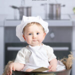 Elle est sympa la photo de ce petit garçon d'un an dans la cuisine du studio. Il porte une petite roque de cuisinier blanc et il est assis dans une grande marmite en cuivre